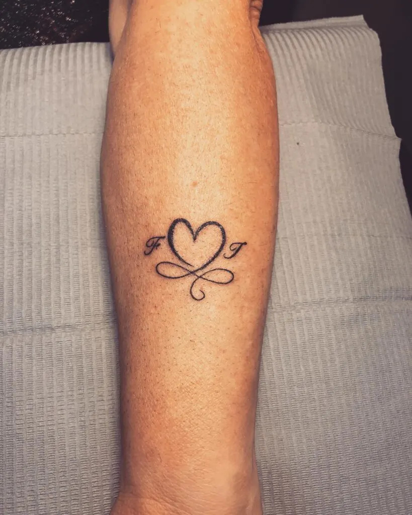 Heart and infinity symbol tattoo with initials, representing eternal love and connection for grandchildren in a minimalist design