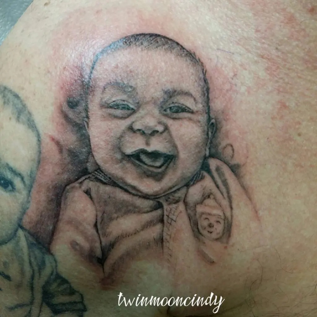 Baby portrait tattoo, depicting a smiling baby to capture the joy and innocence of childhood in a beautiful and personal tribute