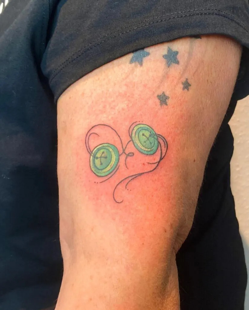Twin buttons tattoo with stars, symbolizing twin grandchildren with green buttons, swirling lines, and the special bond they share with their grandparent