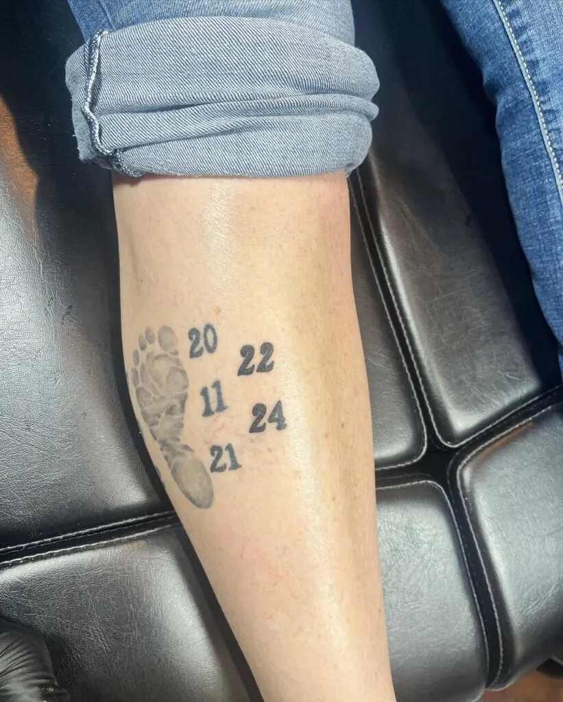 Grandchildren's birth years tattoo, a minimalist design featuring a footprint and birth years, highlighting significant milestones in the grandparent's life