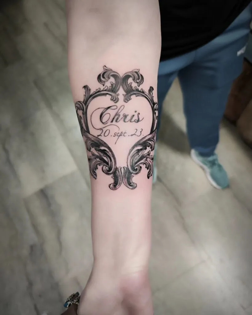 Ornate frame with name tattoo, encircling a name and date with intricate scrollwork, adding elegance and timelessness
