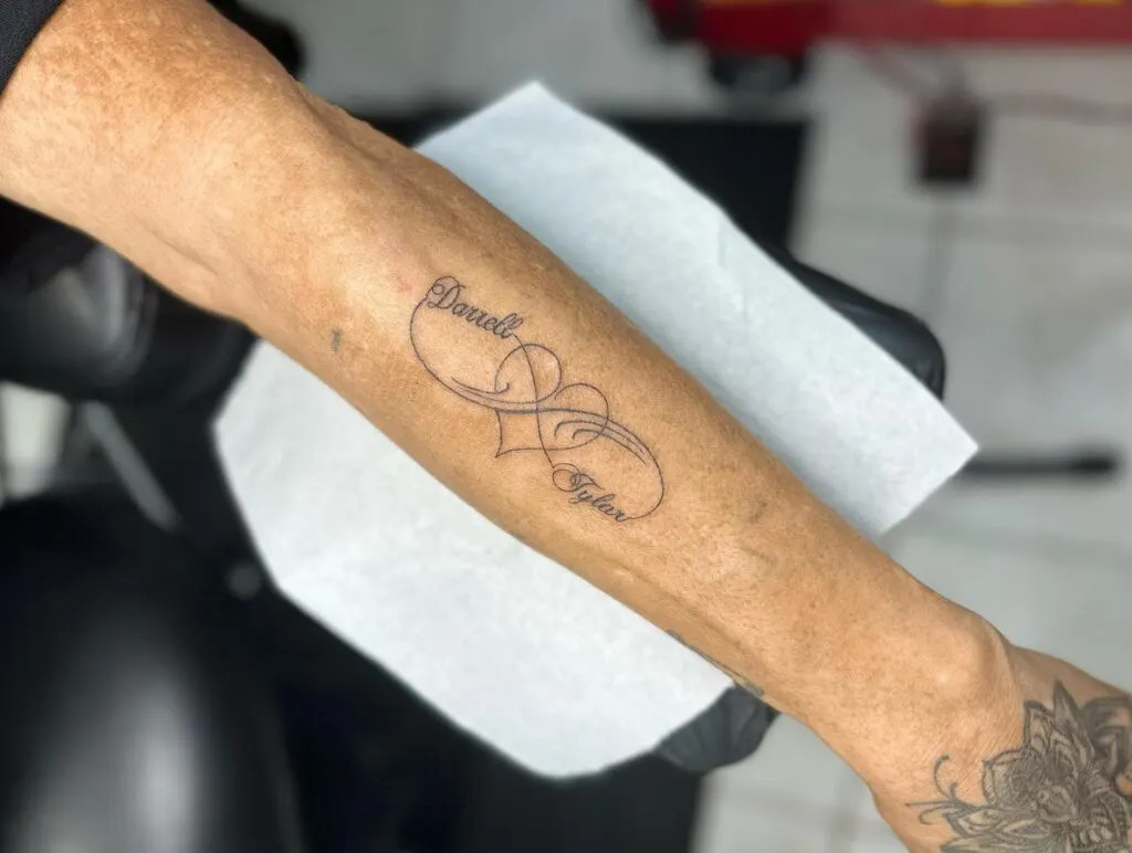 Infinity symbol with names and heart tattoo, symbolizing eternal love and an unbreakable bond with a graceful and personal design