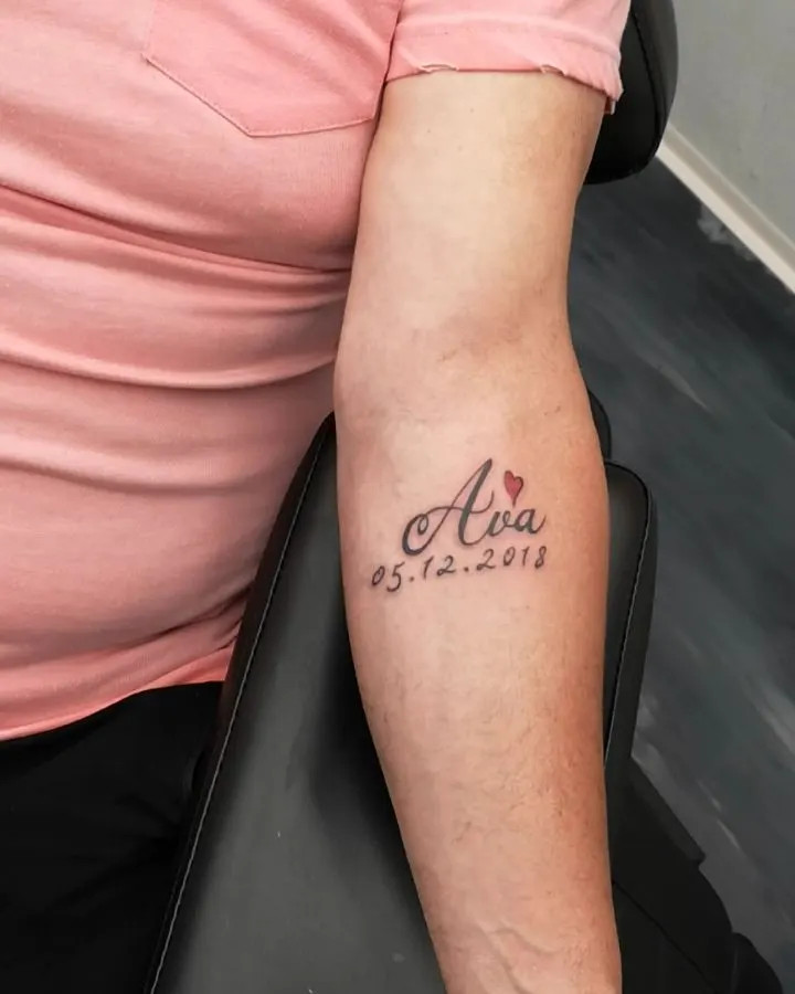 Grandchild's name with birthdate tattoo, a simple yet elegant design highlighting the special bond with a small heart and beautiful script