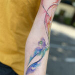 Abstract watercolor tattoo art on shoulder featuring vibrant colors and fluid design