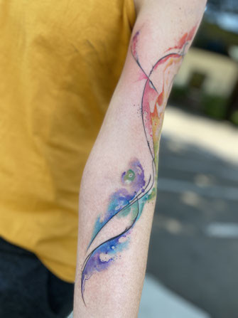 Abstract watercolor tattoo art on shoulder featuring vibrant colors and fluid design