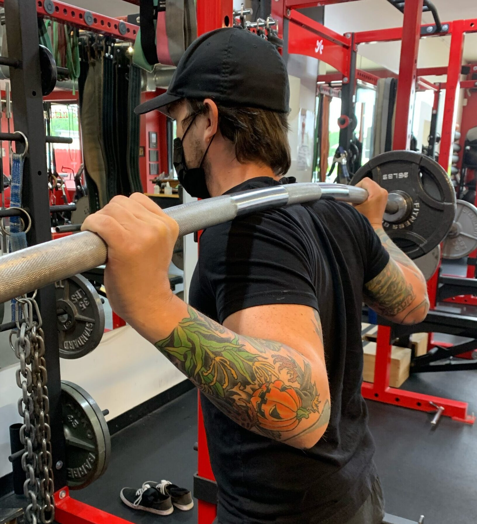 Man with tattoo on his arm and squat bar on his back