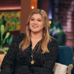 Kelly Clarkson smiling on her talk show, showcasing her vibrant personality and possible tattoo placements
