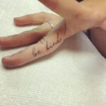 A 'Be Kind' finger tattoo on the side of a woman's finger, serving as a subtle and personal reminder to be kind.