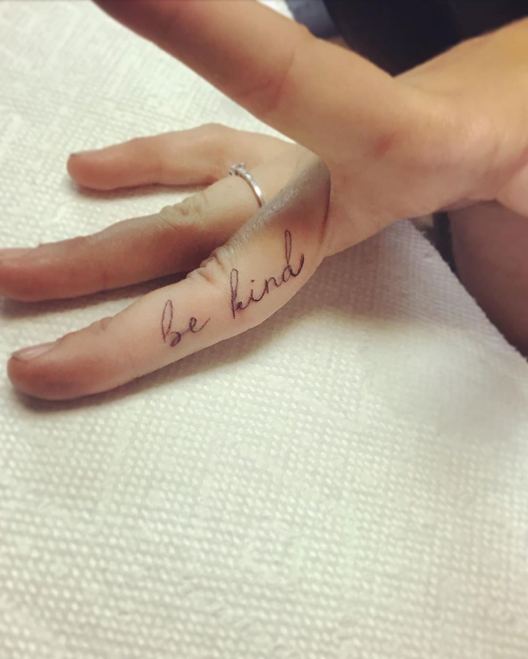 A 'Be Kind' finger tattoo on the side of a woman's finger, serving as a subtle and personal reminder to be kind.