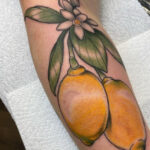 Tattoo of two yellow lemons with leaves and white flower on a arm