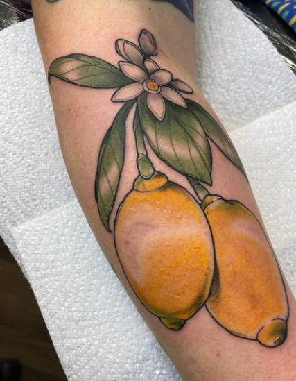 Arm tattoo of two yellow lemons with leaves and a white flower