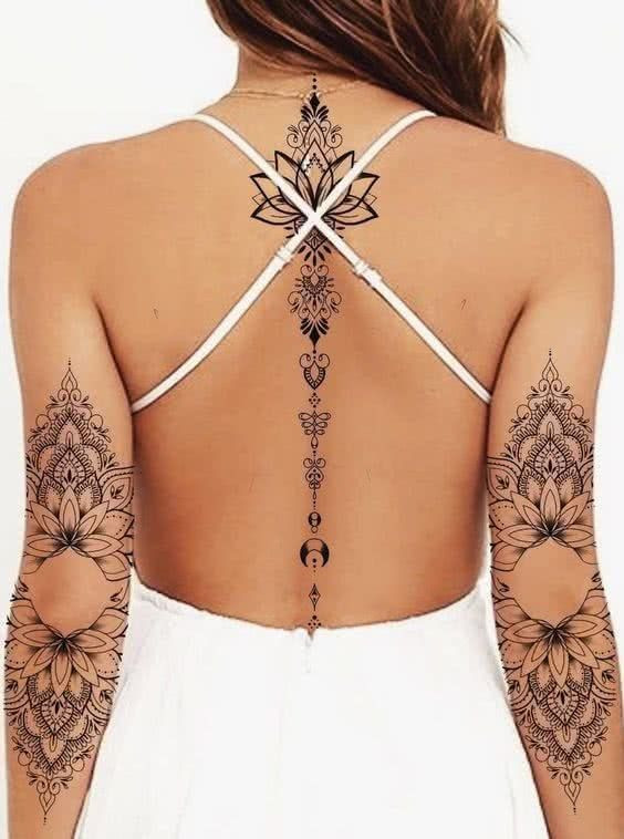 Woman with intricate floral and geometric tattoos on back and arms, wearing a strappy white dress.