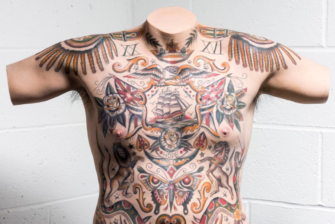 A sailor's torso with multiple tattoos, including a swallow and a ship, illustrating maritime heritage.