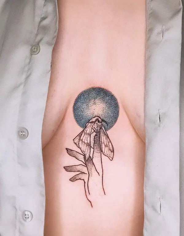 Moth and witchy hand underboob tattoo embracing transformation with magical touch.