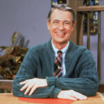 Mr. Rogers in his signature sweater, dispelling the tattoo myth with his gentle demeanor.