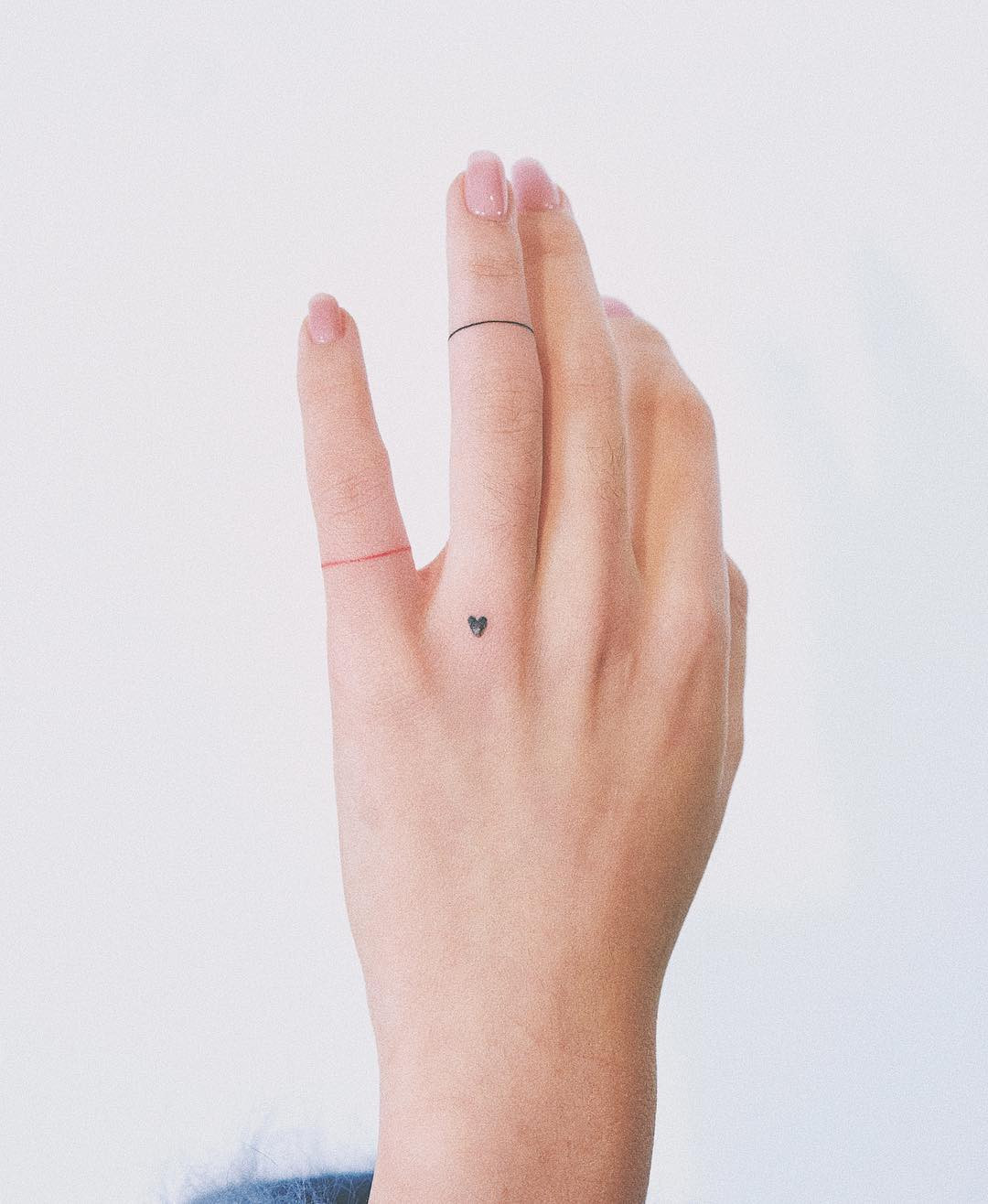 A small heart tattoo on a woman's hand, showcasing a simple yet impactful design.
