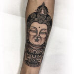 A black and gray Buddha tattoo on an upper arm, showcasing intricate shading and detail