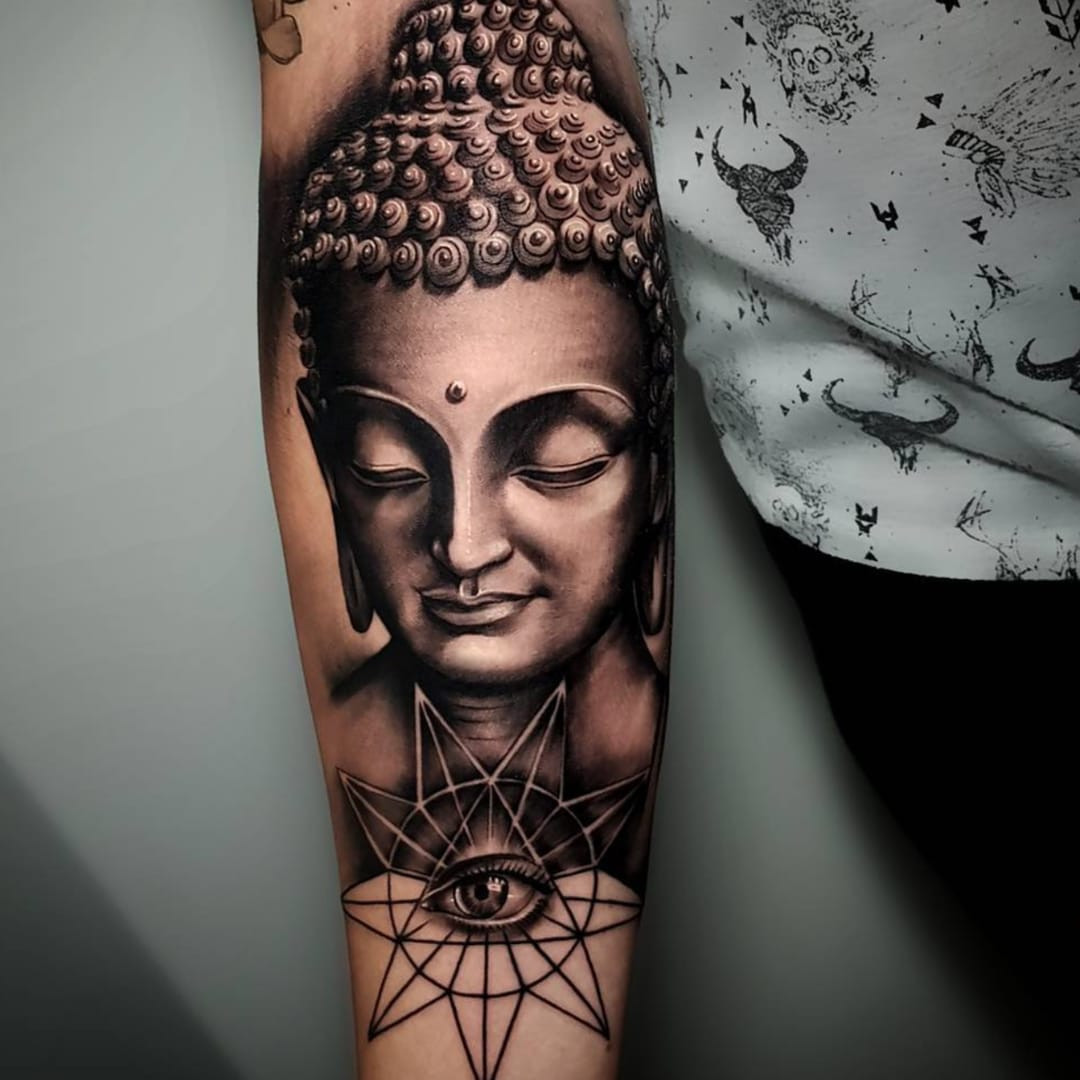 A black and grey Buddha tattoo on a forearm