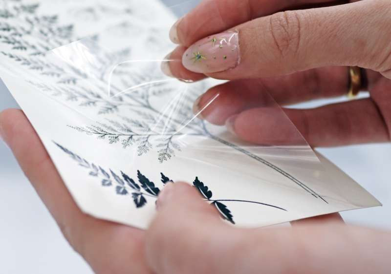 Close-up of a hand peeling back the transparent film from a temporary tattoo before application