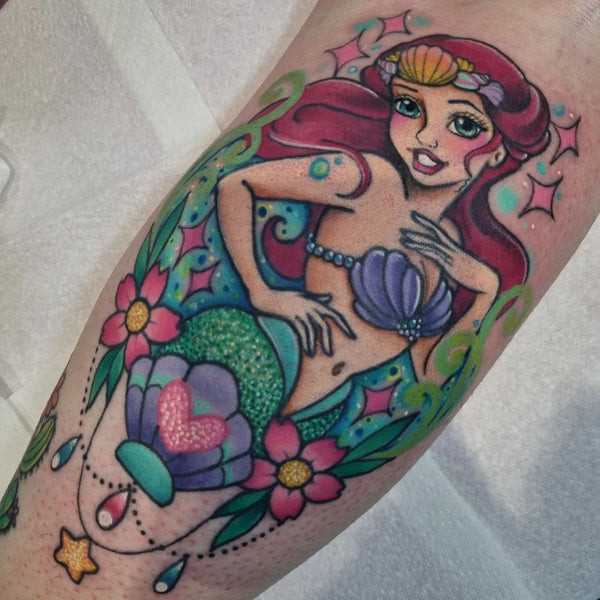 A leg tattoo of Ariel, split into three sessions, showcasing healed lines and fresh color