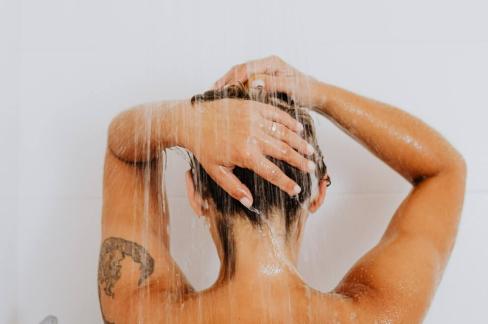 Woman with vibrant arm tattoos standing in a bathroom, gently patting her skin dry with a soft towel after a shower.