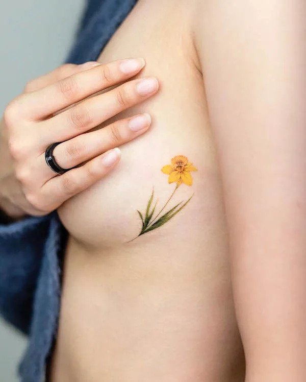 Small yellow flower side tattoo bringing a pop of color and joy.