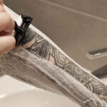 Person shaving their leg with a tattoo