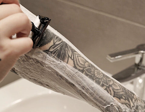 Person shaving their leg with a tattoo