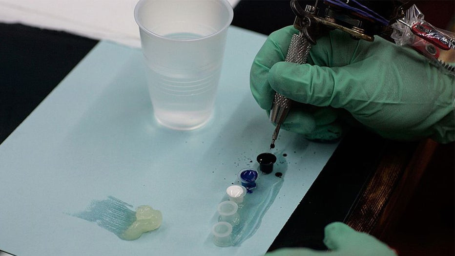A tattoo artist dips his needle in ink