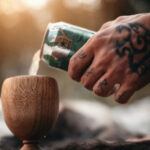 Tattooed Hand Pouring a Beer in a Wooden Cup