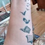 a black and white forearm tattoo of a series of books turning into books and flying away