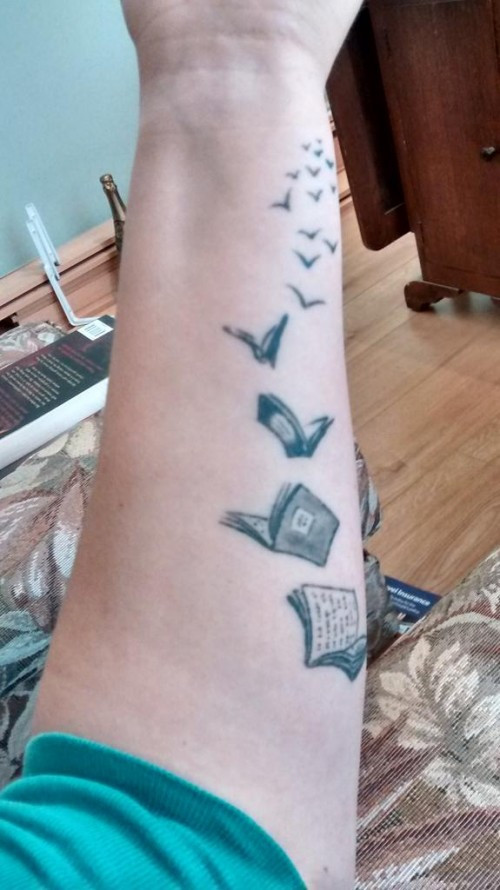 a black and white forearm tattoo of a series of books turning into books and flying away