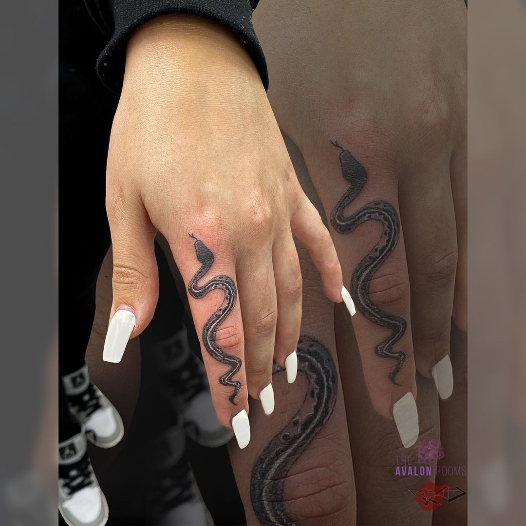 A snake finger tattoo on a woman's finger, symbolizing rebirth, temptation, and power.