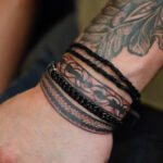 A trio of wrists, each adorned with a delicate silver chain tattoo, symbolizing connection and resilience.