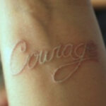 White ink tattoo with intricate floral design on the upper back, demonstrating subtle and elegant body art