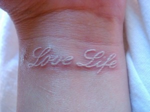 Close-up of a white ink feather tattoo on the forearm, showcasing the fine lines and delicate nature of the design