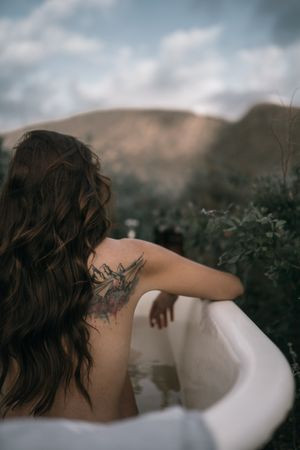Woman relaxing in a bathtub with her tattooed arm carefully positioned out of the water, showcasing how to avoid submerging a new tattoo.