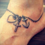 Ankle tattoo of a broken chain connected to a cross, symbolizing freedom and faith