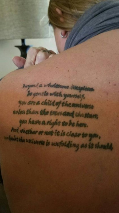 Tattoo on the back of the shoulder with a quote about gentleness and self-acceptance