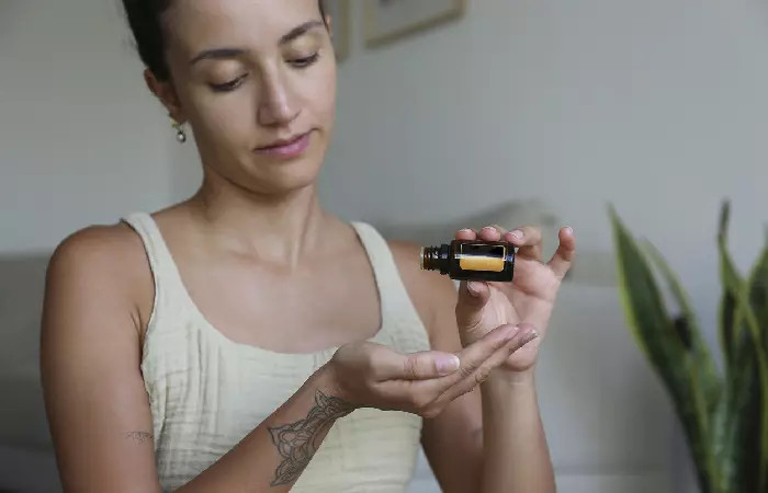 A woman pouring vitamin E oil into her palm to apply on her arm tattoo