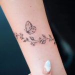 Butterfly and floral bracelet tattoo for women with a flying butterfly detail by @bunami.ink