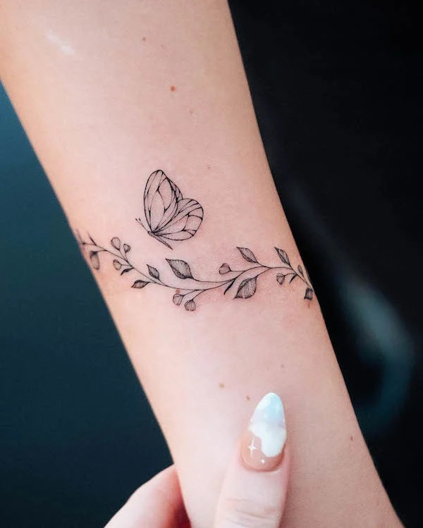 Butterfly and floral bracelet tattoo for women with a flying butterfly detail by @bunami.ink