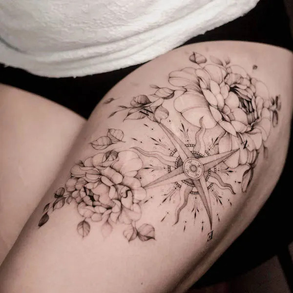 Floral compass tattoo on the thigh, by @dnq.tattoo, combining guidance, intuition, and natural beauty