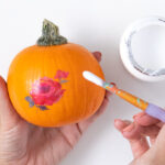 Applying temporary tattoos to a mini pumpkin for a fall decoration
