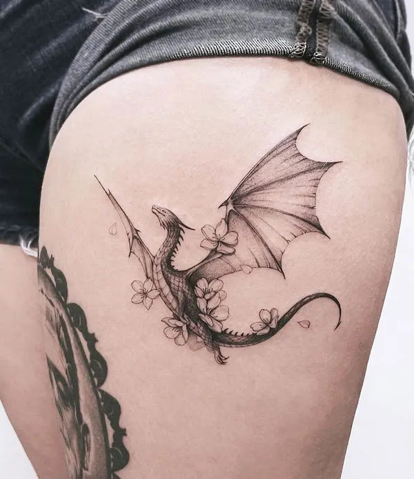Floral dragon tattoo on the thigh, by @baronarttattoo, merging power and beauty in a unique design