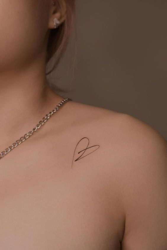 Minimalistic heart tattoo on shoulder, with silver chain necklace. Simple and elegant tattoo design.