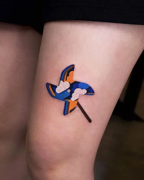 Origami windmill tattoo on the thigh, by @zoonmo, symbolizing childhood memories and hope