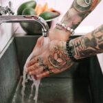 A person carefully washing a new tattoo in the sink.