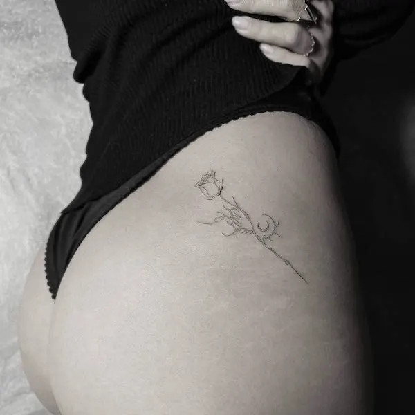 Delicate rose tattoo on the hip and thigh, by @jakenowicz, representing subtle beauty and grace