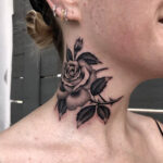 Rose tattoo on neck with leaves detail; the dark lines and shading contrast with the wearer's light skin.